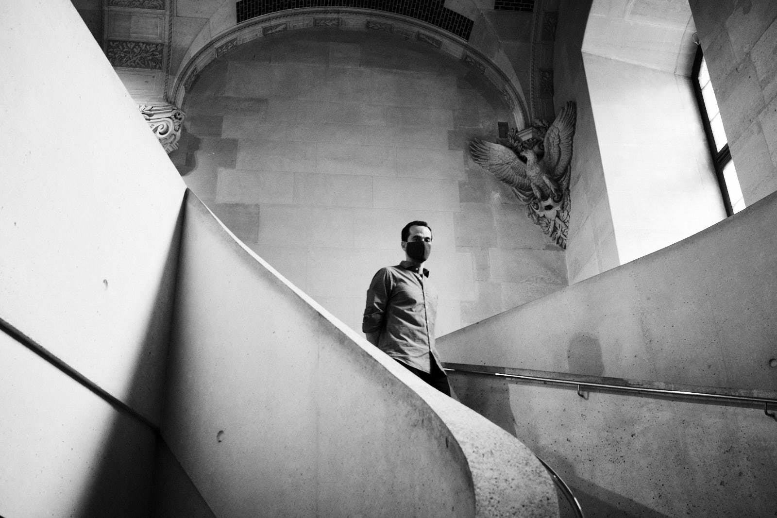 man with face mask on stairs at the louvre museum in paris
