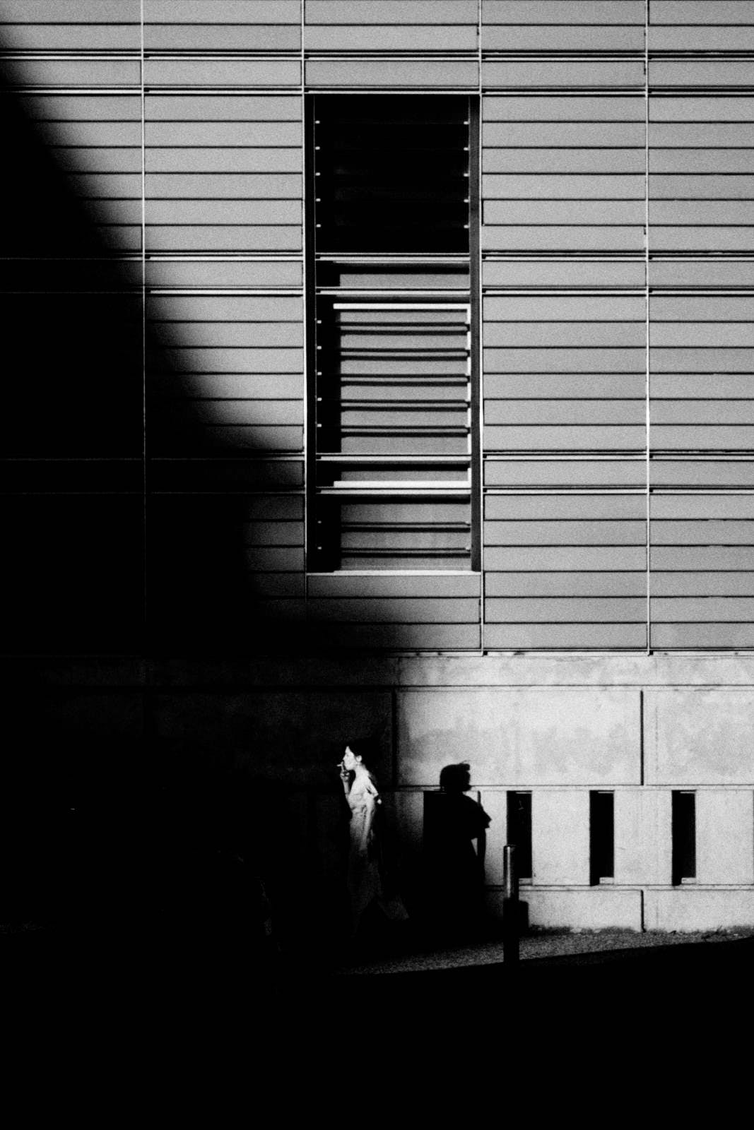 girl smoking in front of a wall with a window and shadows